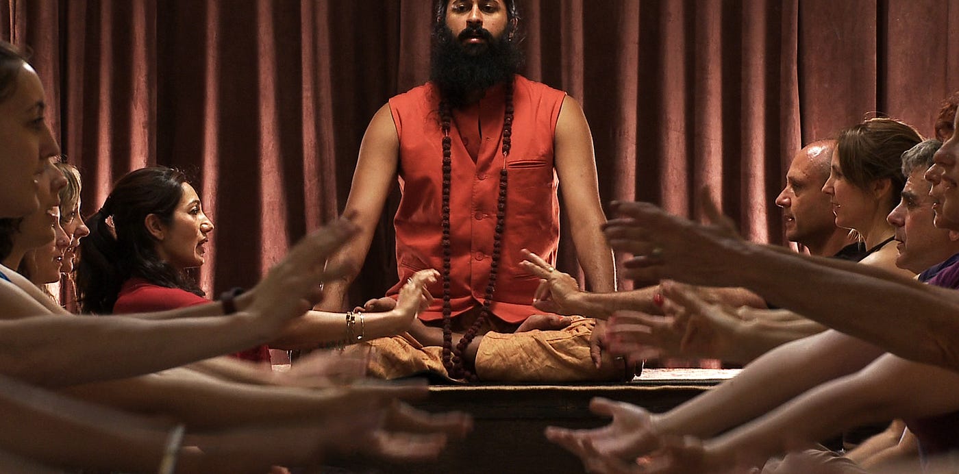 Screenshot from the documentary Kumaré showing the filmmaker in the role of a guru surrounded by followers.