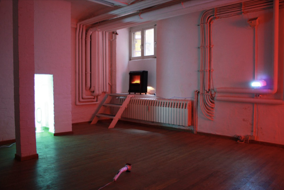 IN & OUT, 2004/2013 — room with heating devices, pink ambient light, exposed piping, and a glowing threshold