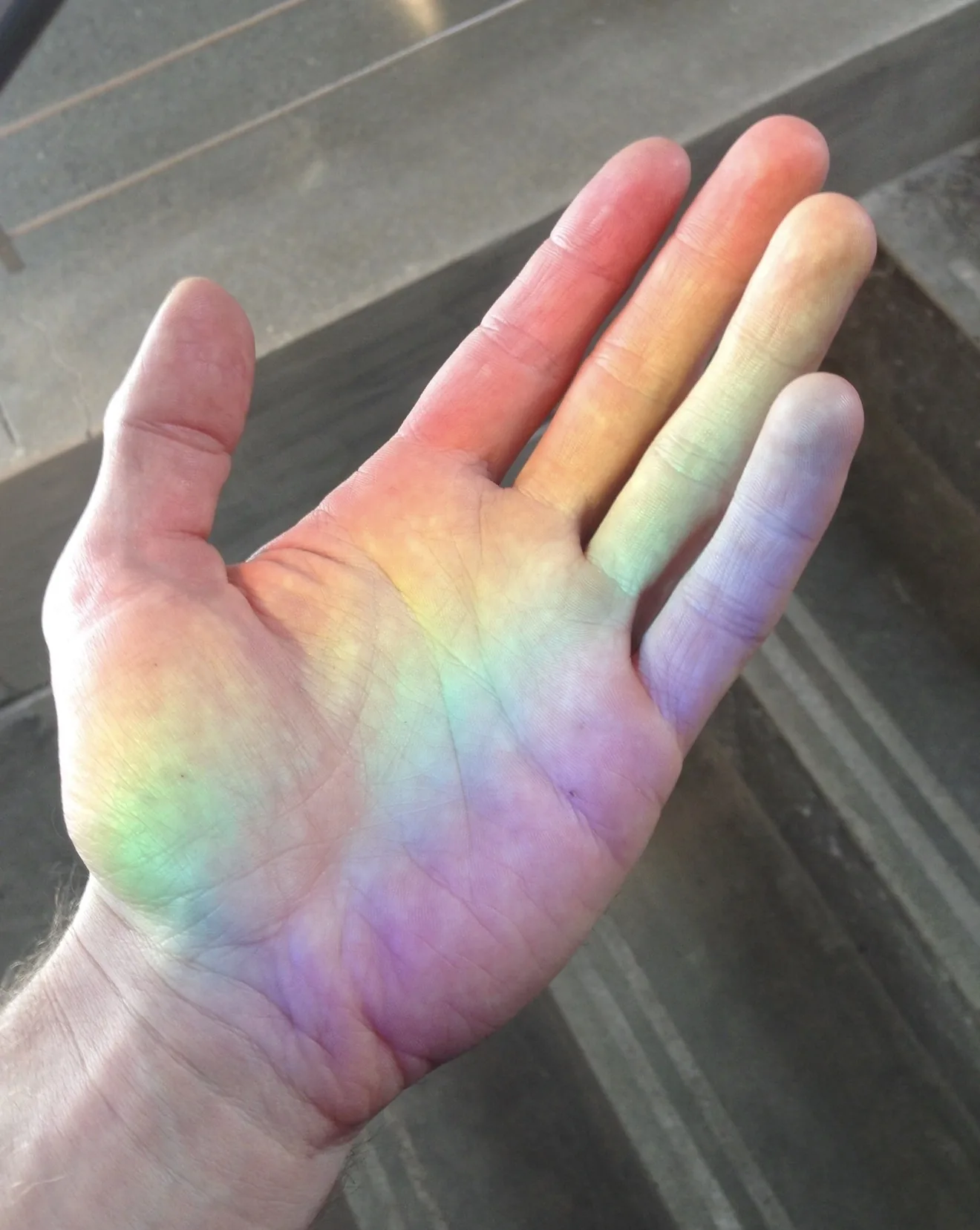 Open human hand crossed by bands of red, orange, yellow, green, blue, and violet light