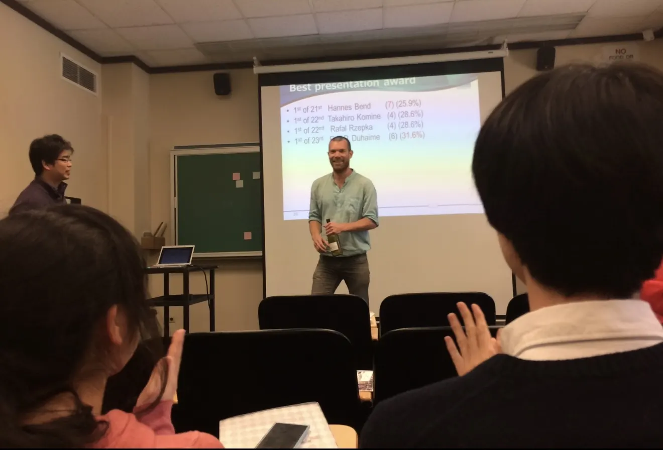 Hannes Bend speaking beside a projected Best Presentation Award slide at AAAI 2016.