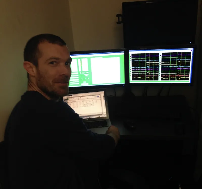 Hannes Bend at an EEG monitoring workstation displaying multichannel brain-wave traces, University of Oregon.
