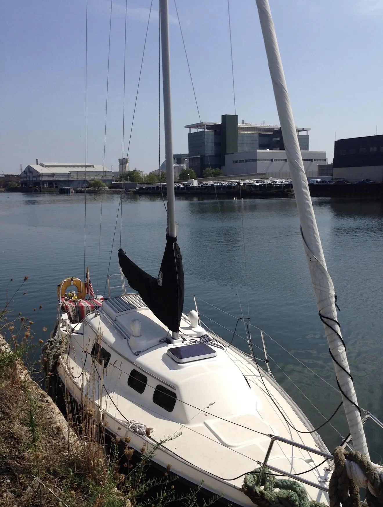 Hannes Bend's sailboat moored on Newtown Creek in daylight, with industrial buildings on the far bank.