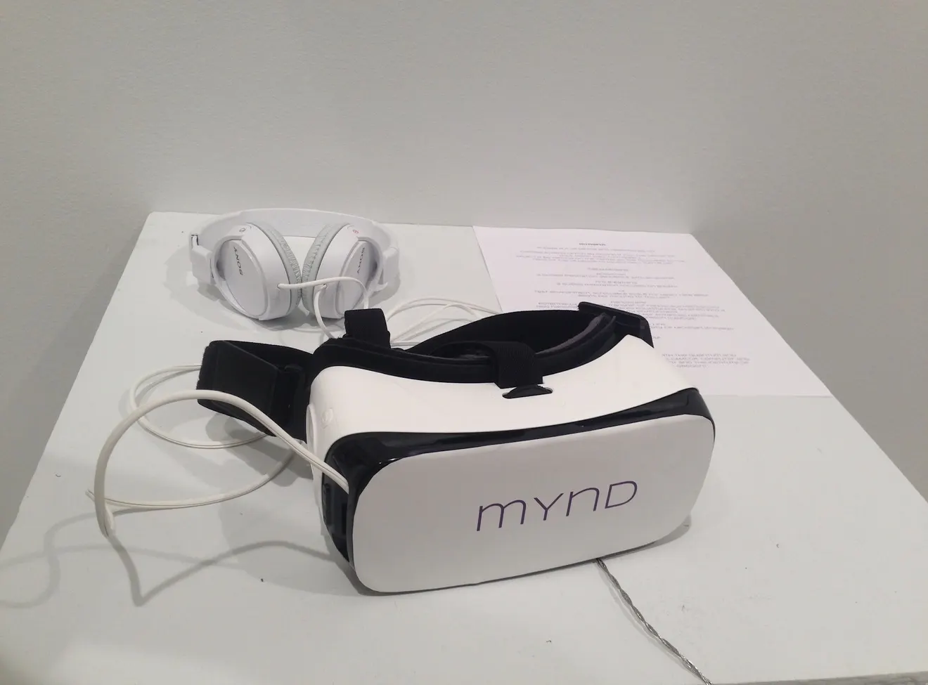 VR headset, headphones, cables and a printed sheet arranged on a white display plinth.